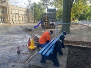 A blue buddy bench being bolted to the ground at Leal Elementary School by a facilities worker.