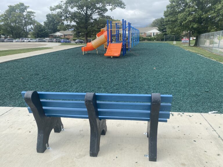 The back of a blue buddy bench outside of the playground at Thomas Paine elementary.