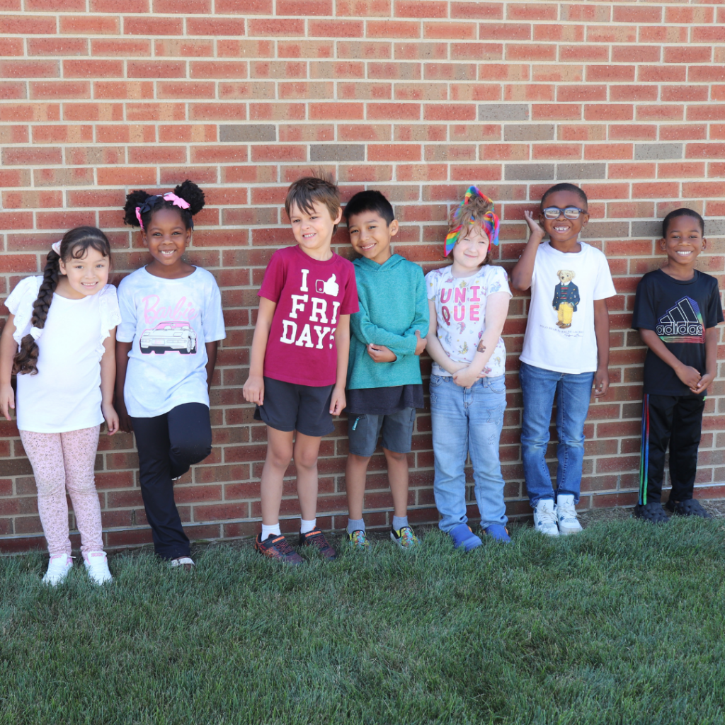 Students lined up outside front of a brick wall on the grass for a photo.
