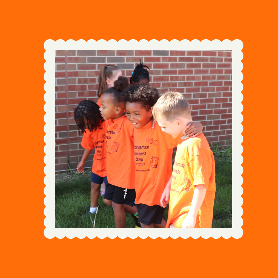 Four students in orange shirts walking with their arms around each other.